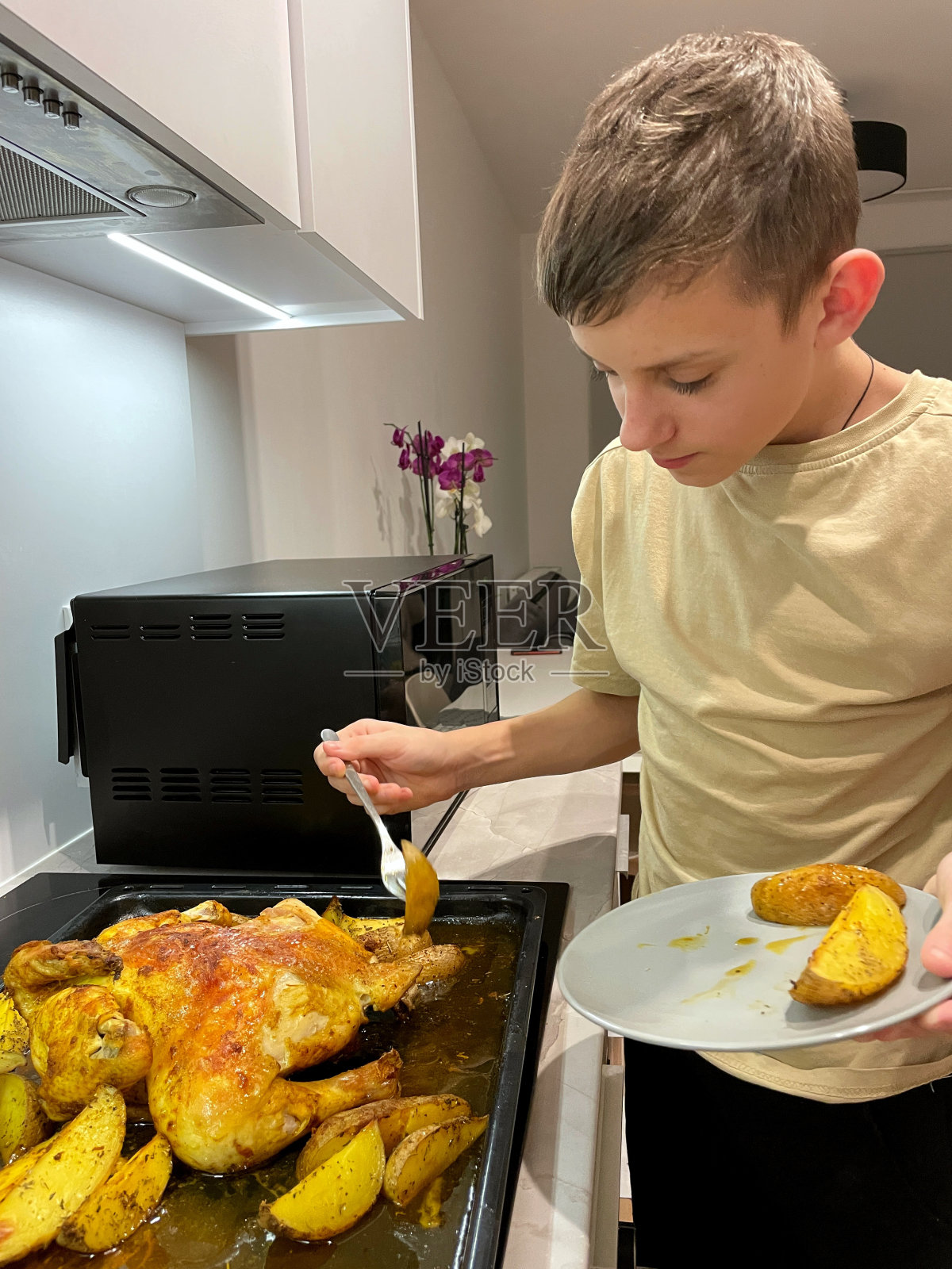 一个十几岁的男孩在厨房里品尝烤鸡和土豆照片摄影图片
