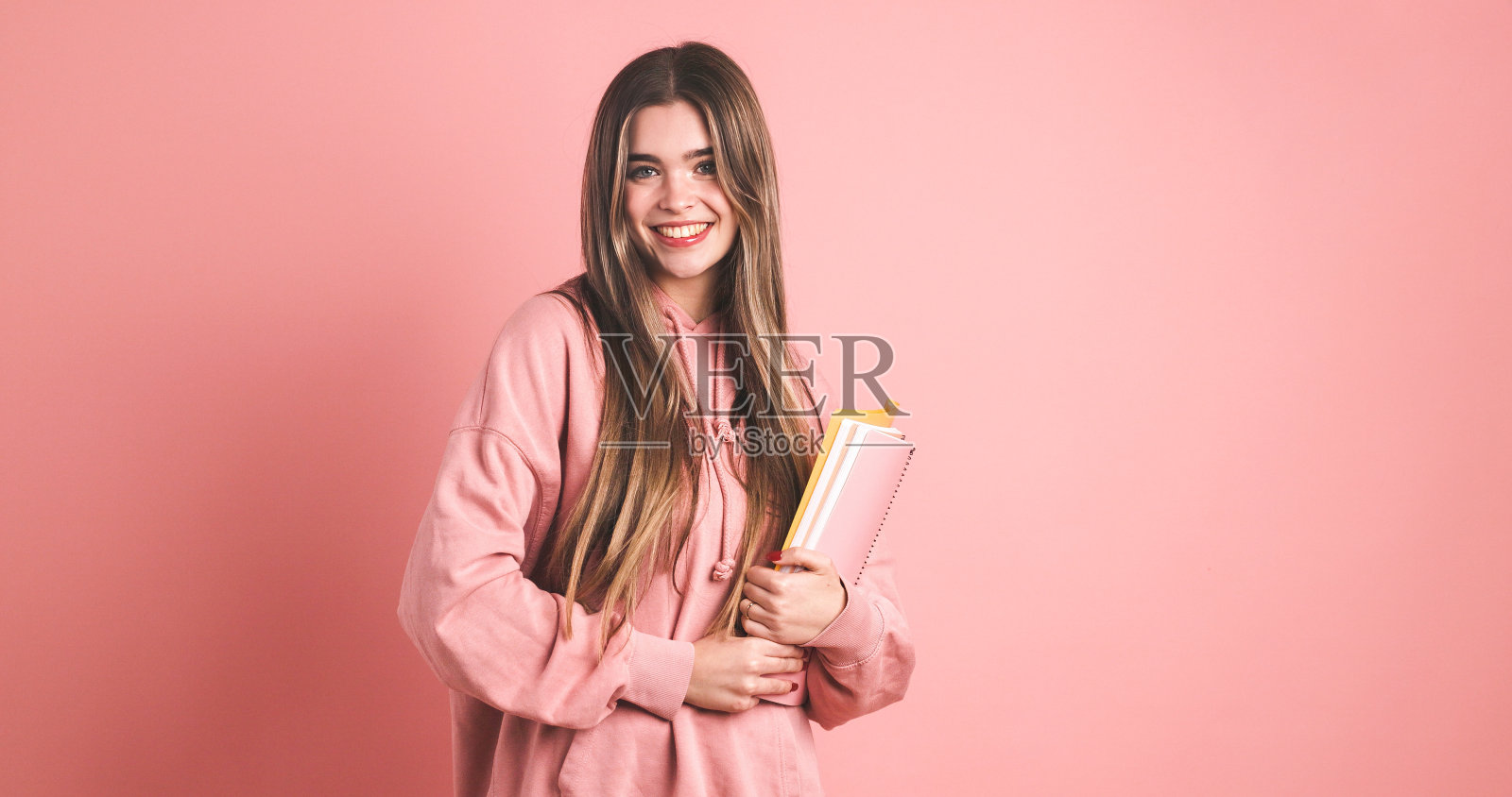 快乐的女大学生背着双肩包，拿着粉红色的书照片摄影图片