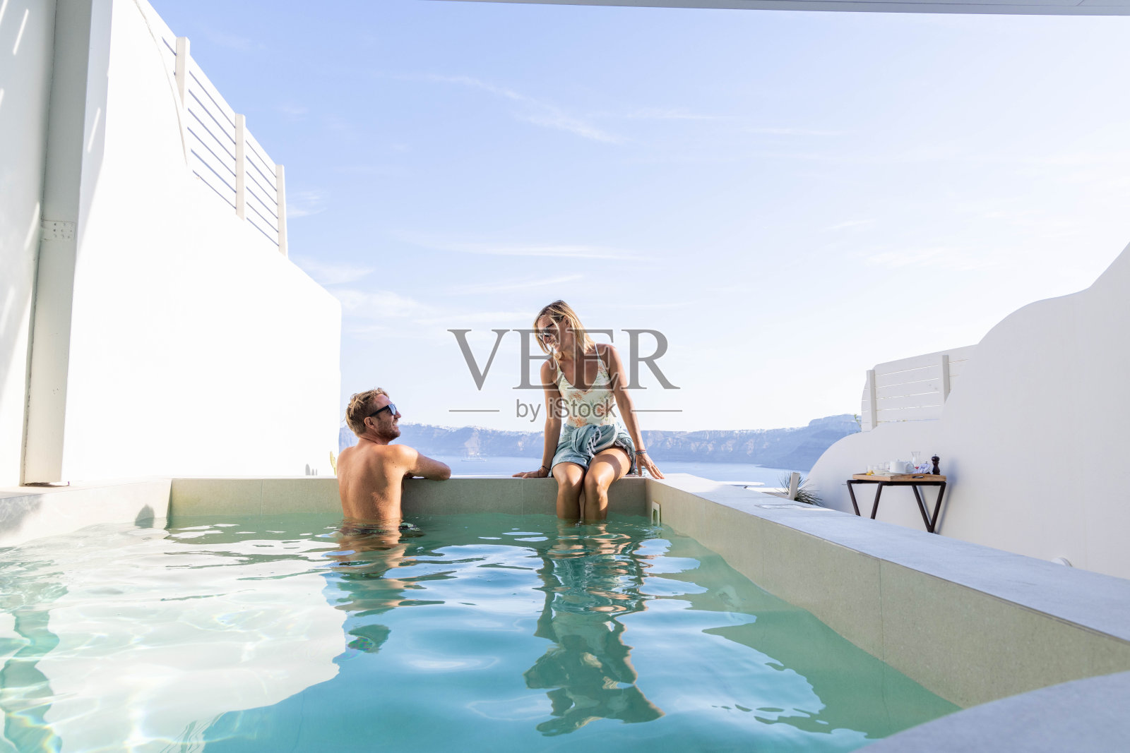 池畔和谐:夫妇放松的私人别墅游泳池与风景秀丽的海景照片摄影图片