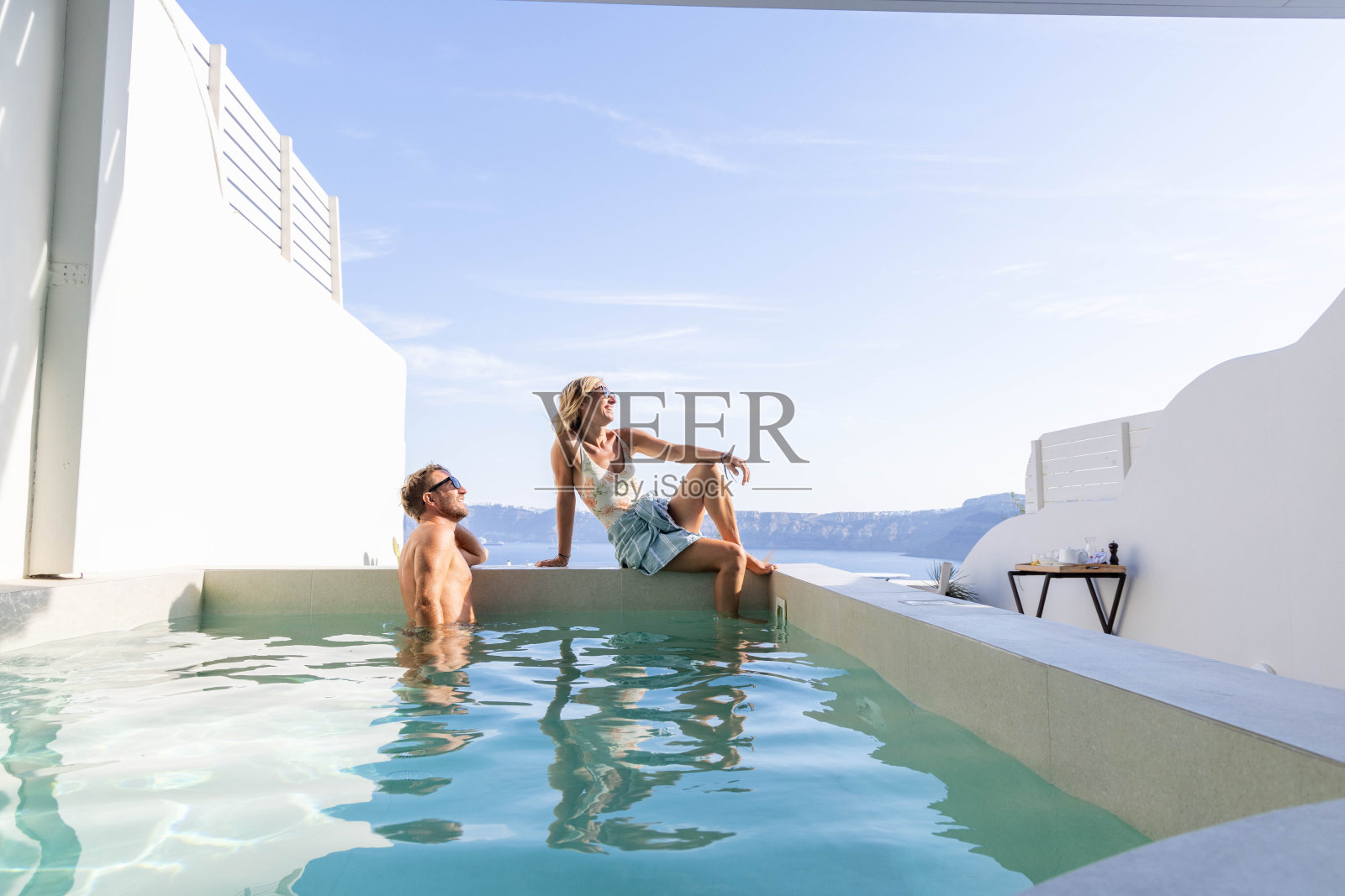 池畔和谐:夫妇放松的私人别墅游泳池与风景秀丽的海景照片摄影图片