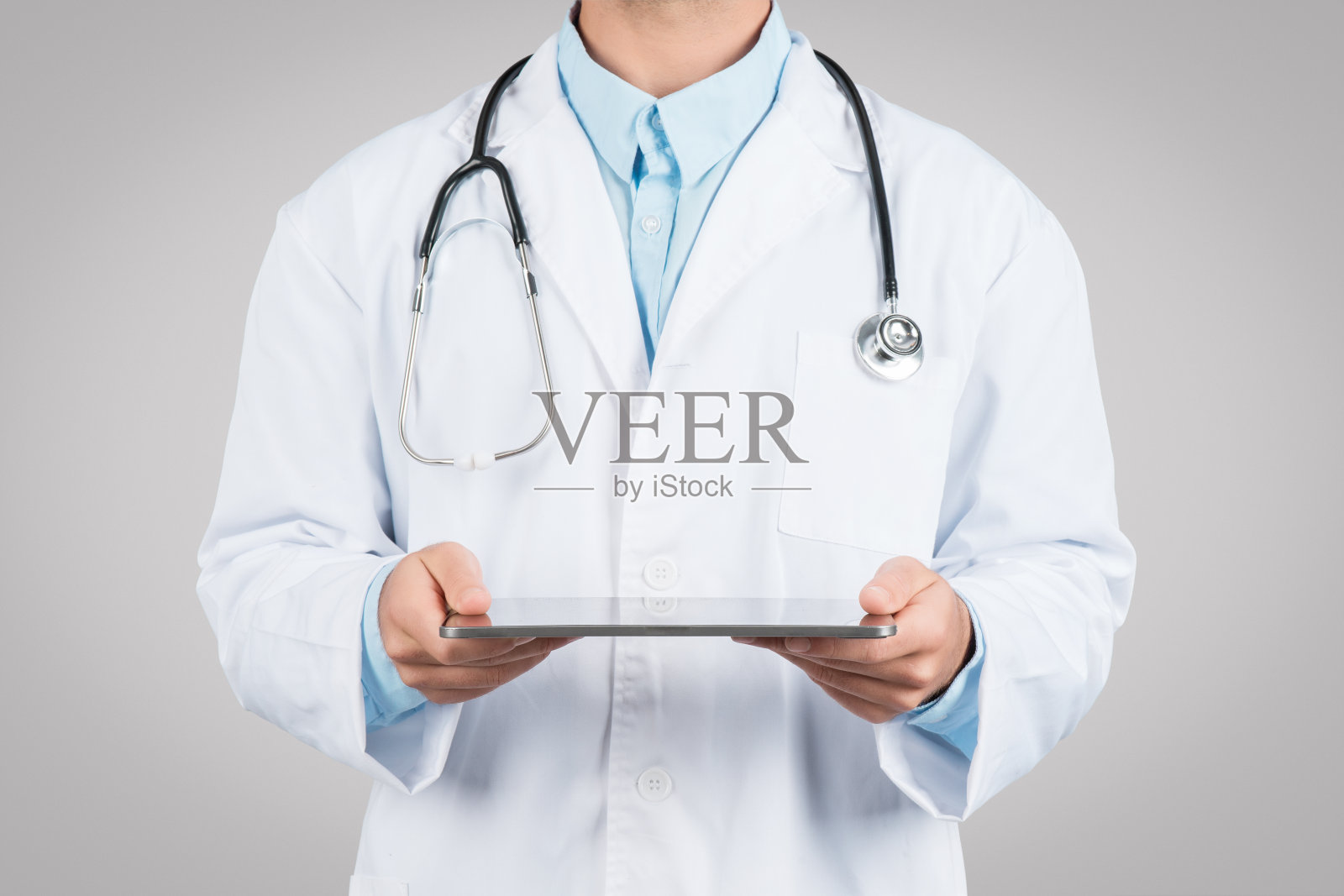 医药和技术。无法辨认的男医生使用数码平板电脑，站在灰色的工作室背景上照片摄影图片