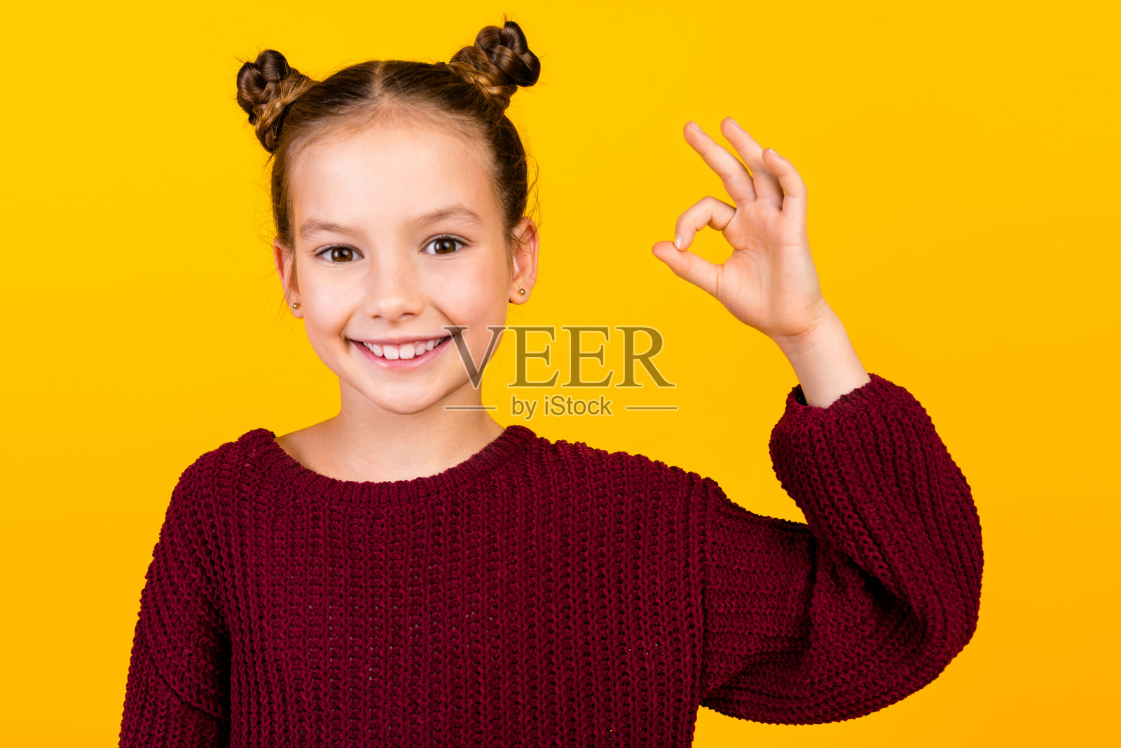 可爱的小学生的肖像，微笑着手臂的手指，在黄色的背景上展示了ok的符号照片摄影图片