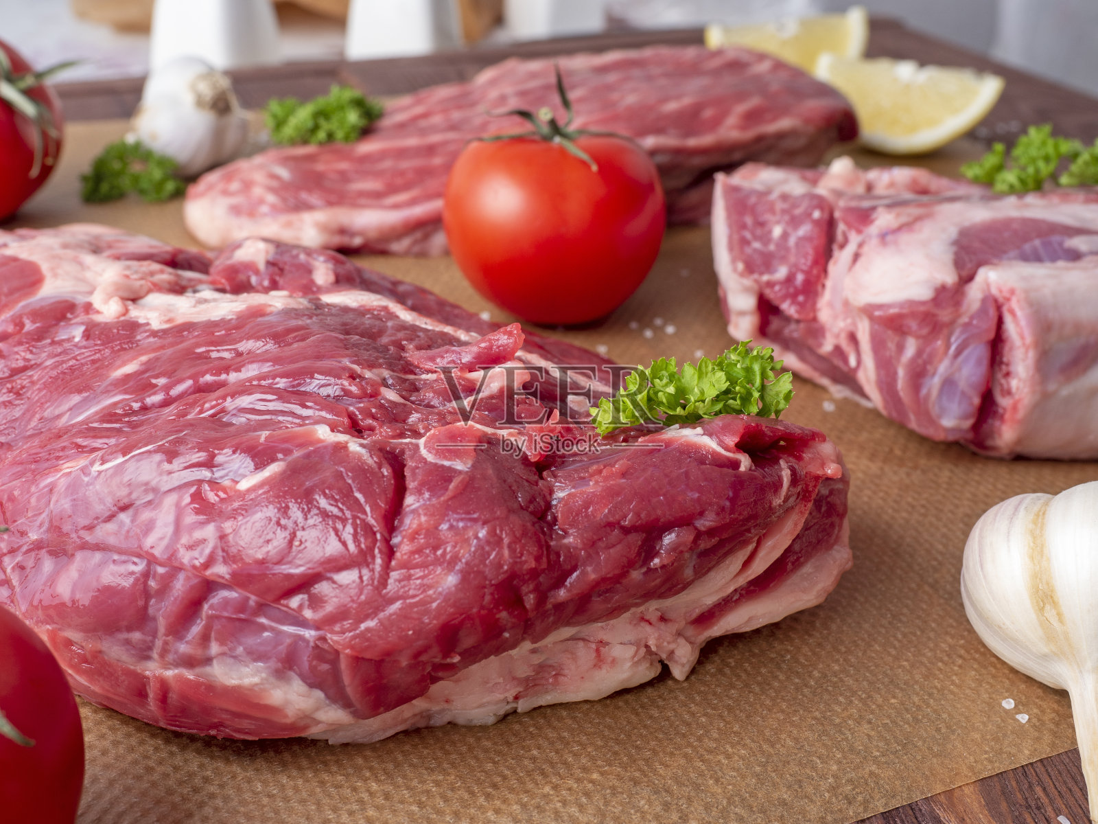 羊皮纸上放着几块带有大理石花纹的黑色安格斯牛肉，周围是绿色植物和蔬菜。侧视图。照片摄影图片