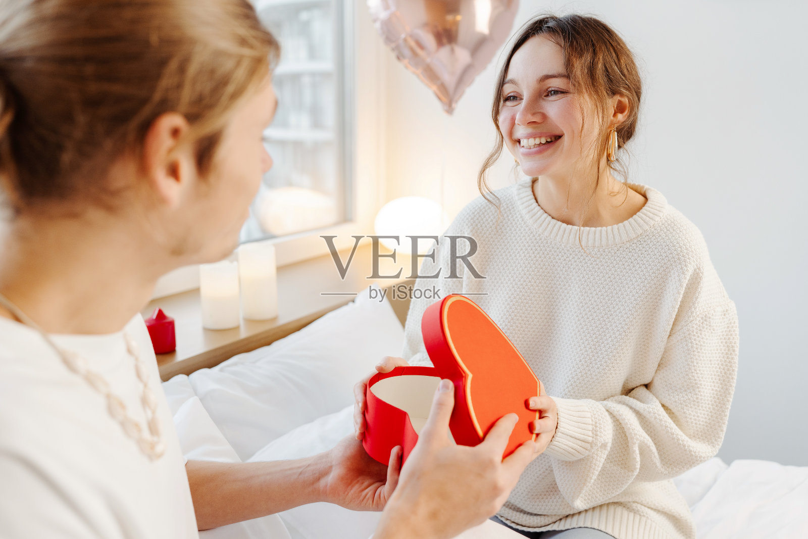 美丽，微笑的女人在家里的卧室里打开红色的礼盒，那是她男朋友送的礼物照片摄影图片