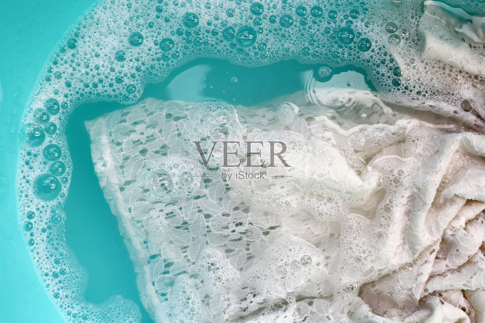 女士的蕾丝裙浸泡在水中，溶解洗涤剂有白色的泡沫。衣服的概念照片摄影图片