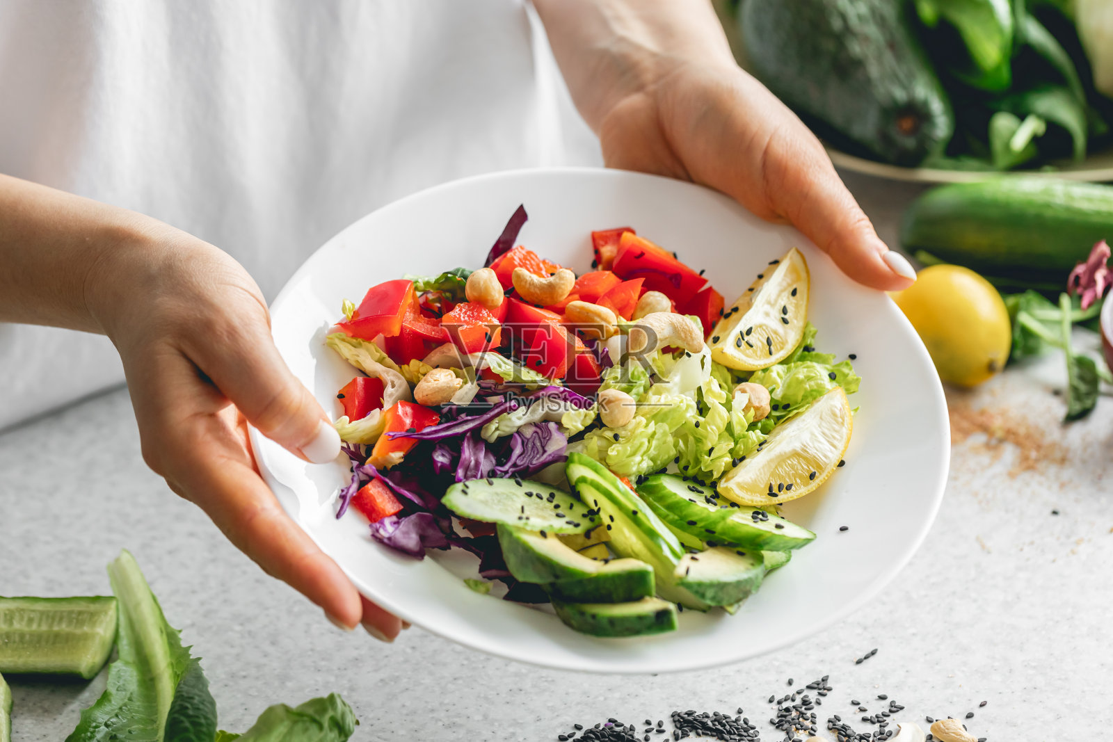 厨房里，一个女人手里拿着一盘切碎的新鲜蔬菜。照片摄影图片