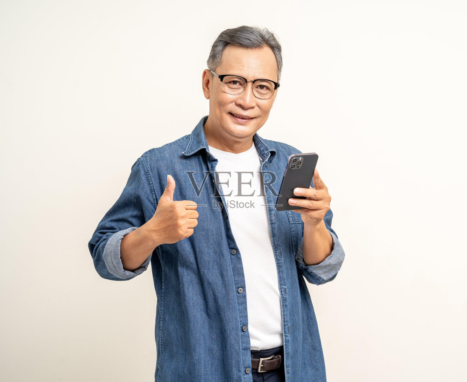 英俊的亚洲成熟老人站在孤立的白色背景上使用智能手机。欢快微笑的亚洲高级男子手持手机的幸福肖像。成熟的人和生活方式照片摄影图片