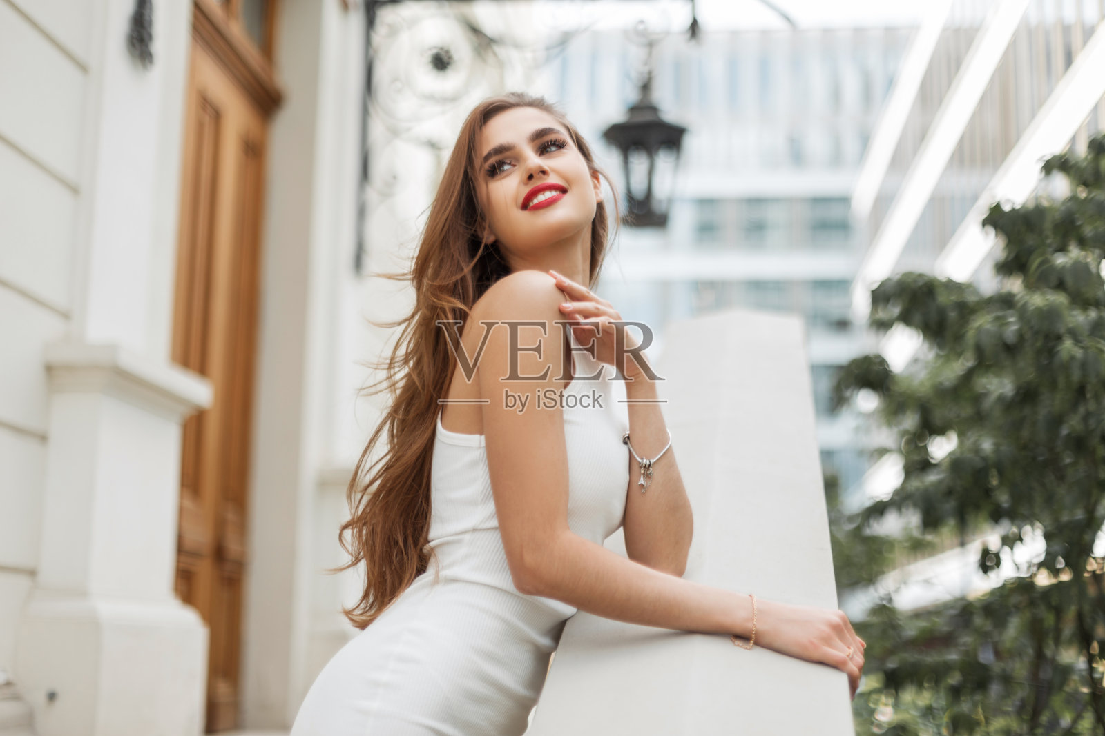 快乐美丽优雅的模特女孩，红唇，穿着时尚的白色连衣裙，站在户外，享受着古老的建筑照片摄影图片