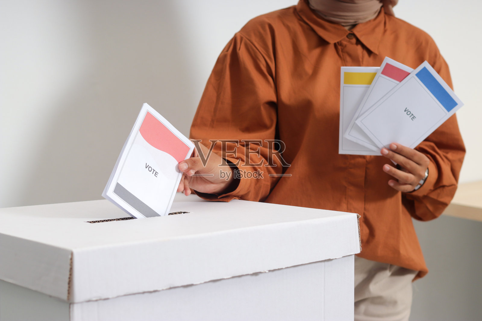 一名戴头巾的亚洲妇女将选票插入投票箱。印度尼西亚总统和政府的大选或Pemilu。白色背景上的孤立图像照片摄影图片