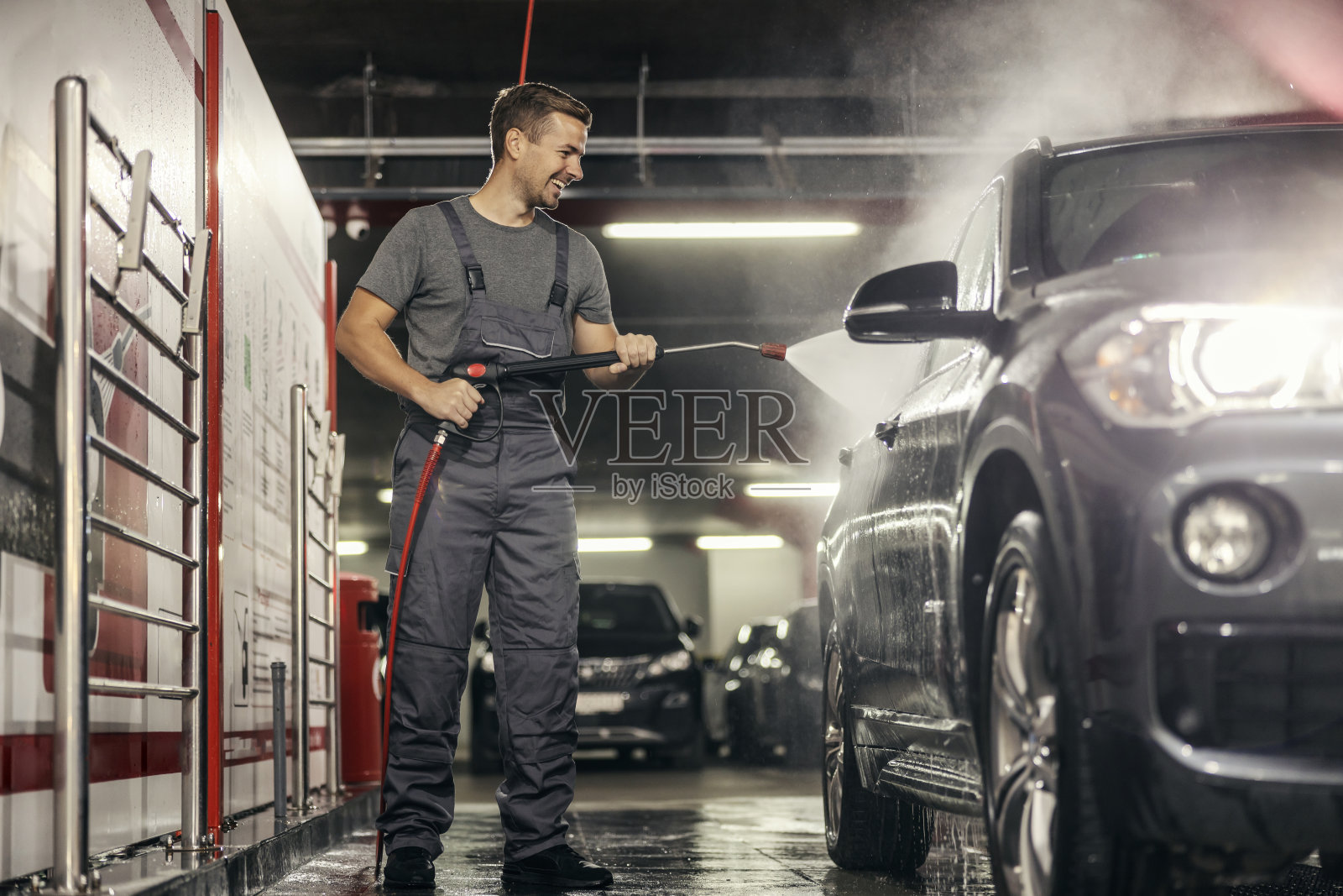 洗车站的工人在高压水枪下洗车。照片摄影图片