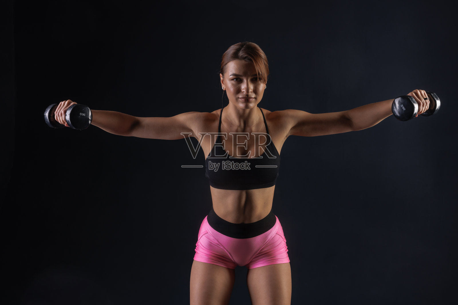 运动女孩用黑色背景的哑铃做运动，运动概念照片摄影图片
