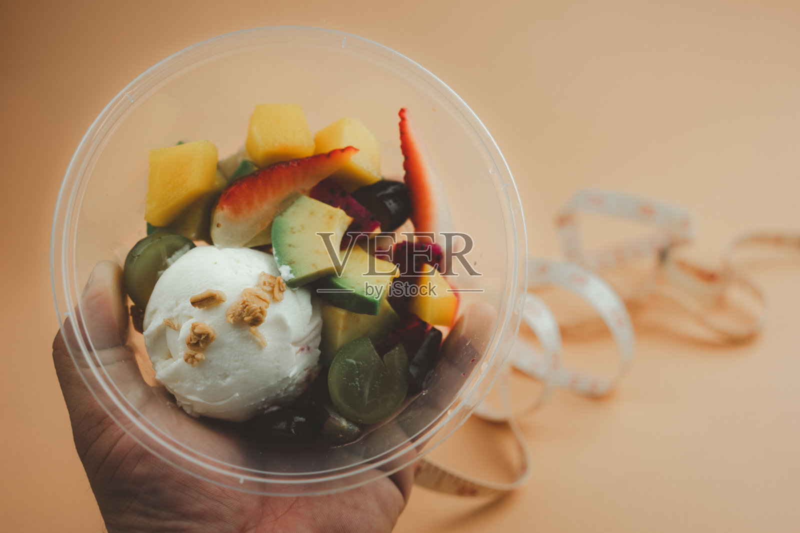 午餐盒里装满了水果和酸奶，手里拿着白色的卷尺，背景模糊不清照片摄影图片