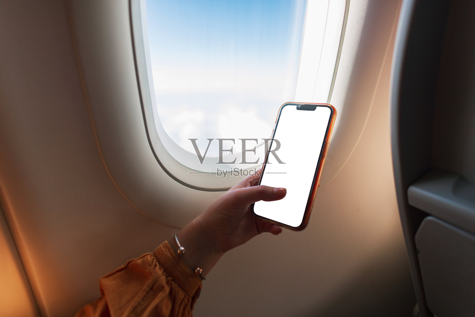 女孩坐在飞机上，手里拿着一个手机模型。商务、旅行和工作。女性使用智能手机照片摄影图片