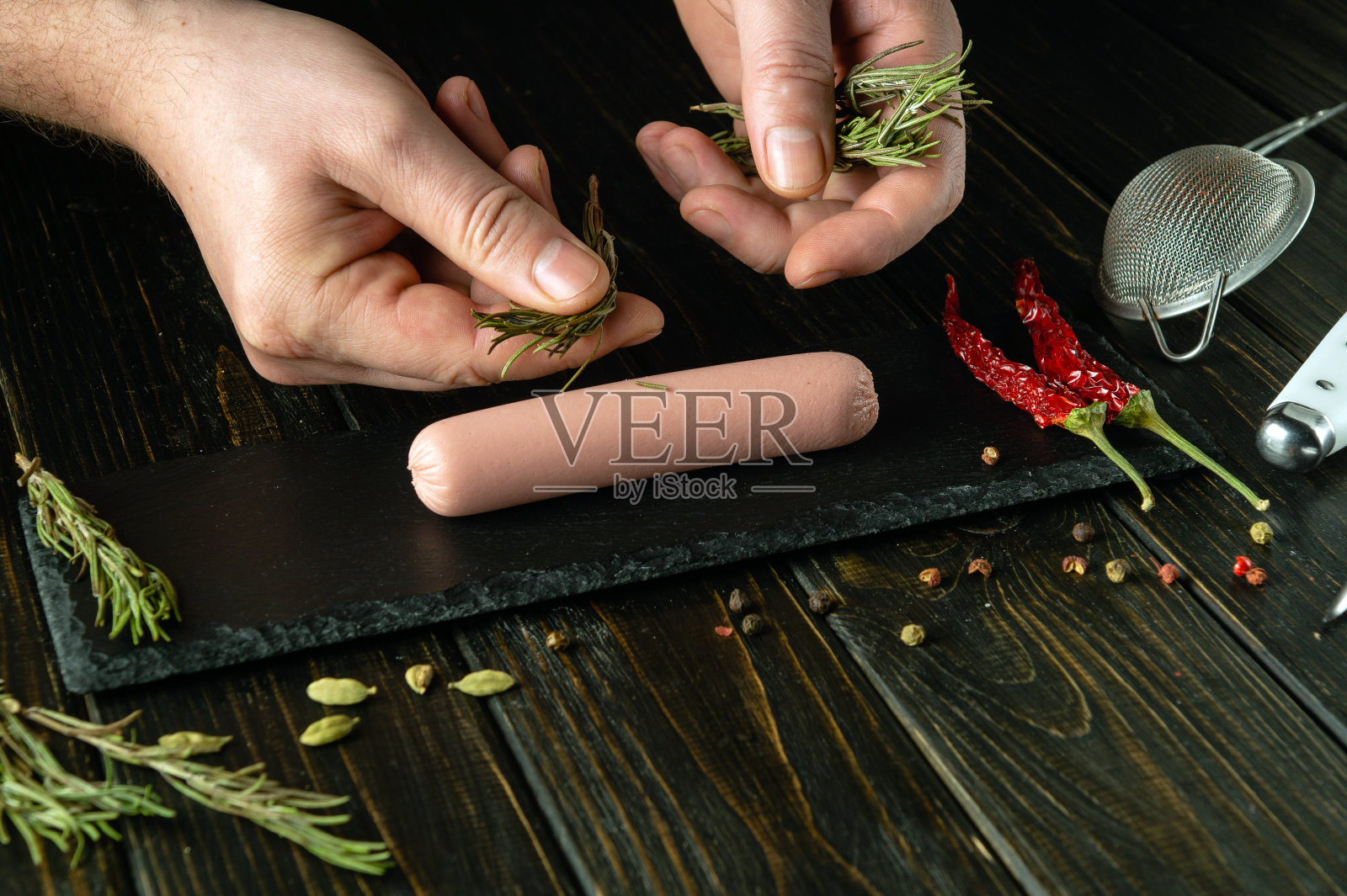 厨师在厨房的桌子上煮多汁的香肠。在烤香肠之前加入迷迭香。提供美味晚餐的概念照片摄影图片