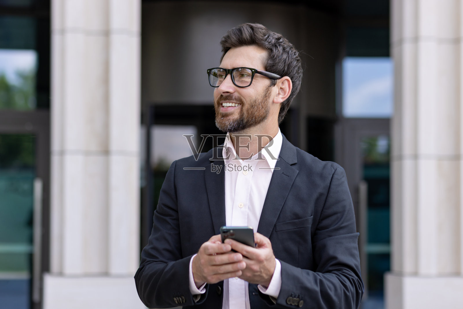 自信的商人留胡子在城市办公大楼外使用智能手机照片摄影图片