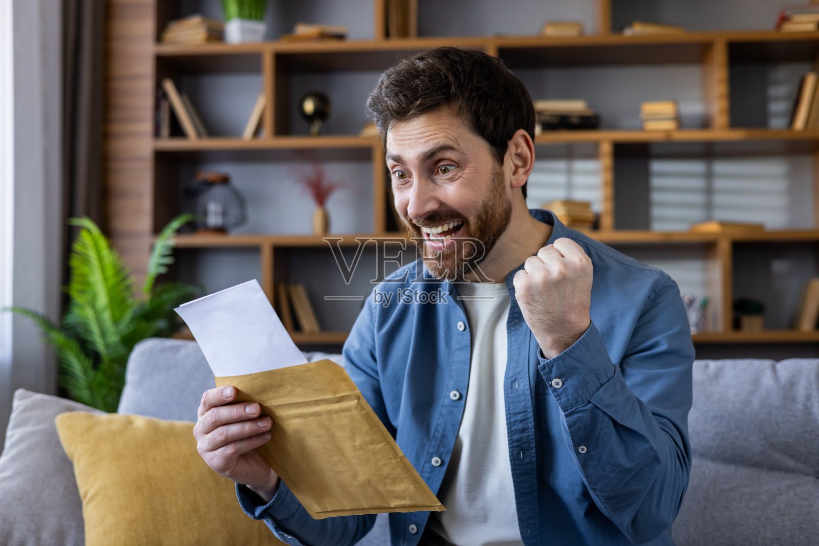 兴奋的男人在家里庆祝好消息，手里拿着信封照片摄影图片