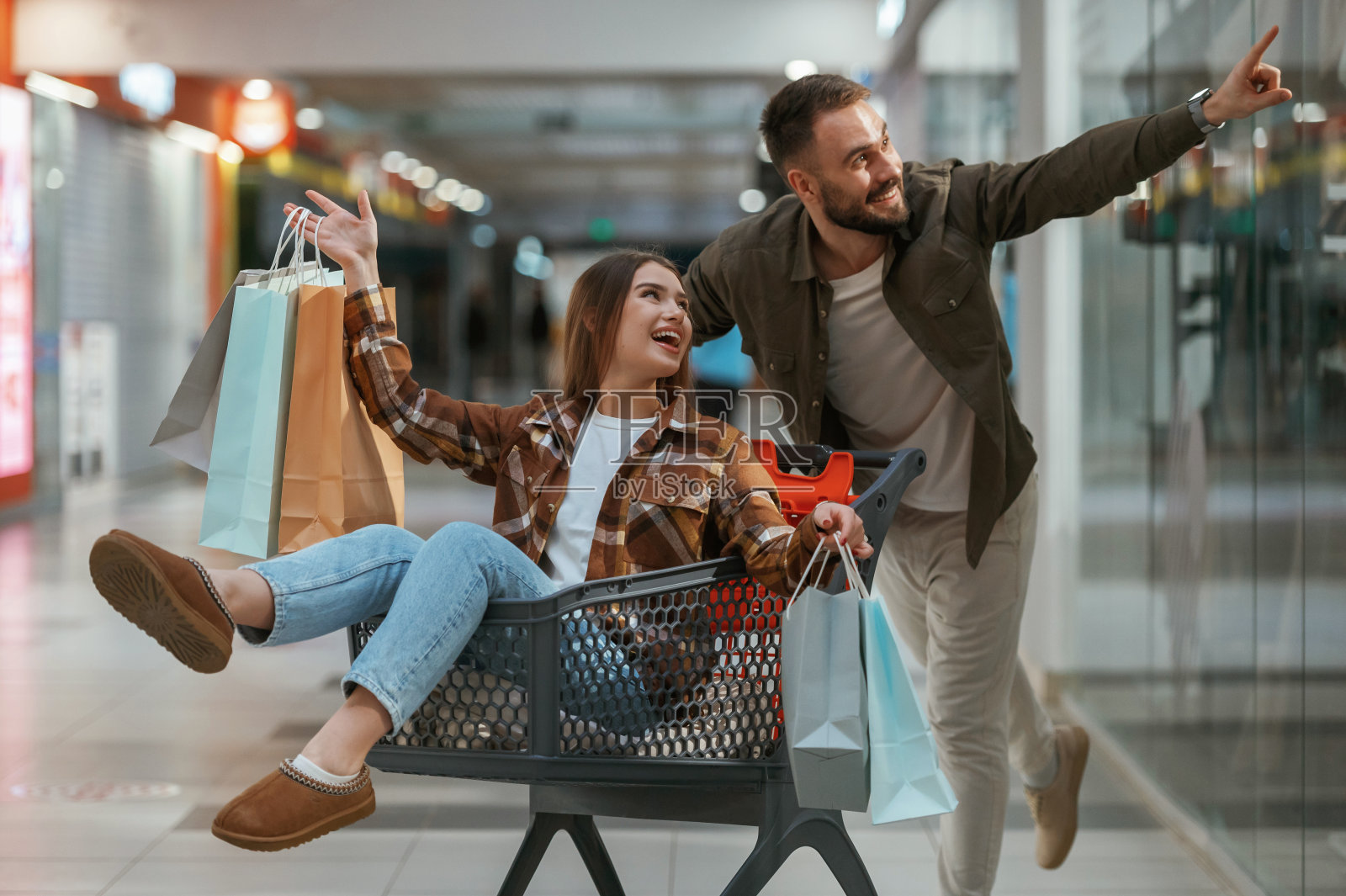 在购物中心玩得开心，骑着购物车。一对年轻的夫妇一起在超市照片摄影图片