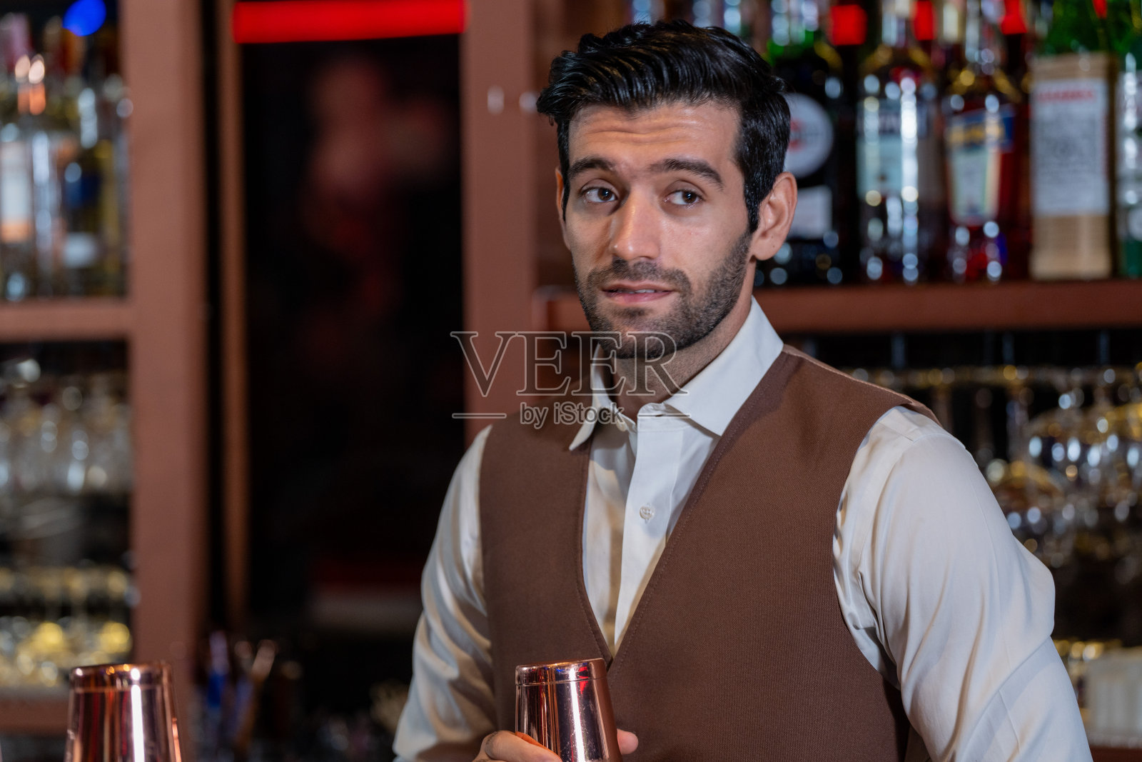 男酒保正在酒吧里调制饮料并跳舞。有一群人跳舞的舞会。女人和男人在夜总会喝着马提尼鸡尾酒，玩得很开心。照片摄影图片