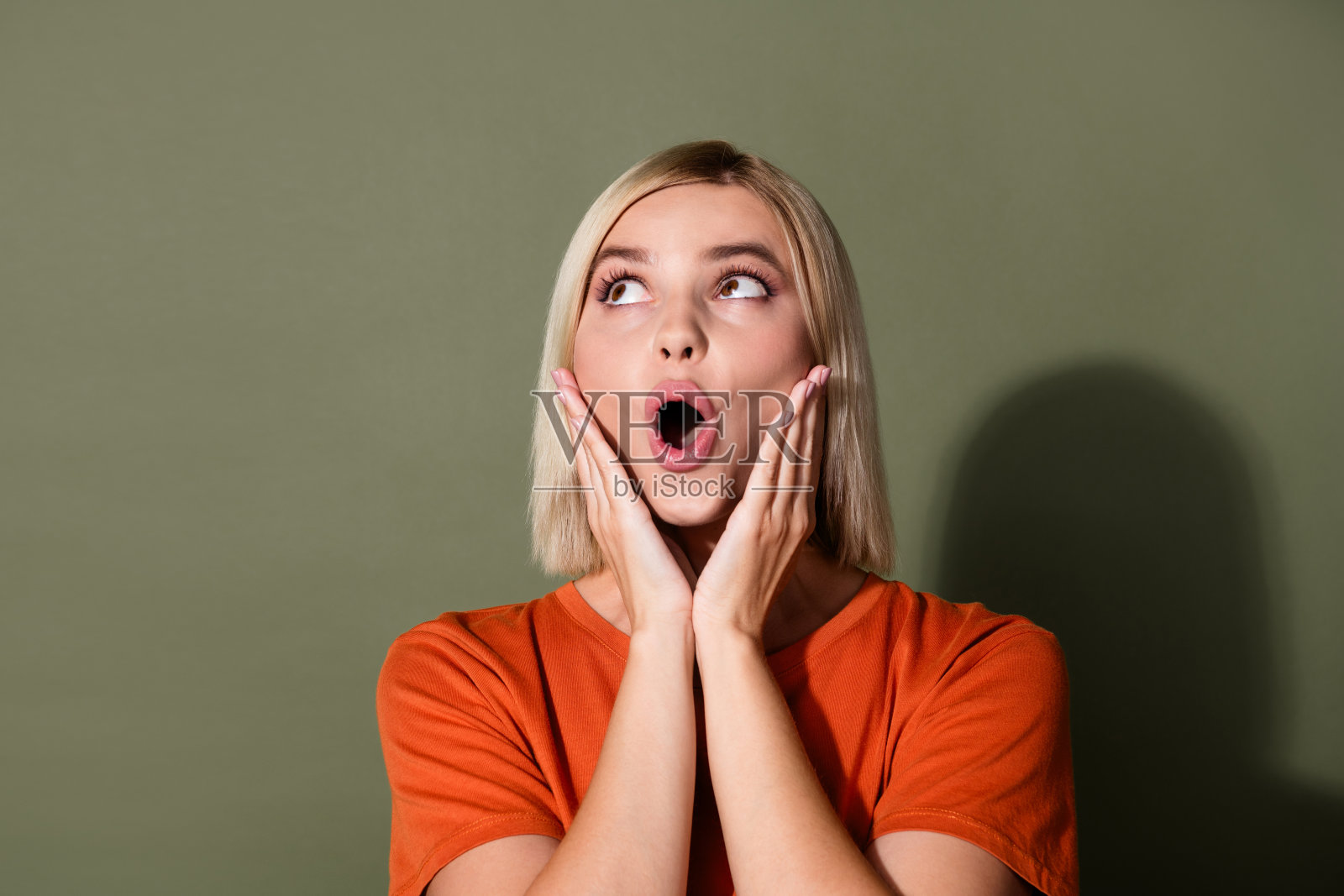 照片肖像可爱的年轻女士脸颊，双手看起来空白空间震惊穿着时髦的橙色服装孤立在卡其色的背景照片摄影图片