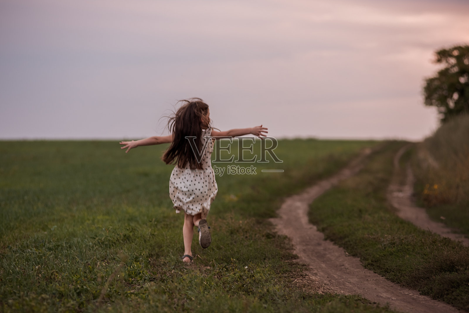 穿着裙子的长发小女孩跑过绿色的田野。活泼有趣的童年。周末旅行照片摄影图片