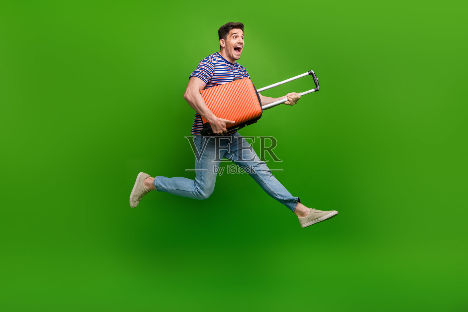 全尺寸照片印象深刻的家伙穿着牛仔裤条纹t恤跑在度假与袋孤立的绿色背景照片摄影图片