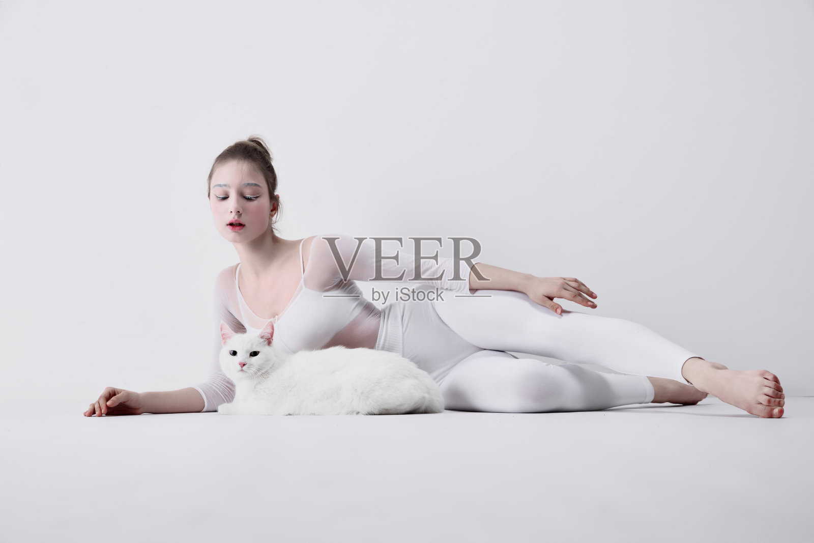 提倡与宠物和平共处的健康品牌活动。在白色的工作室背景下，穿着白色衣服的年轻女子温柔地与一只白猫互动照片摄影图片