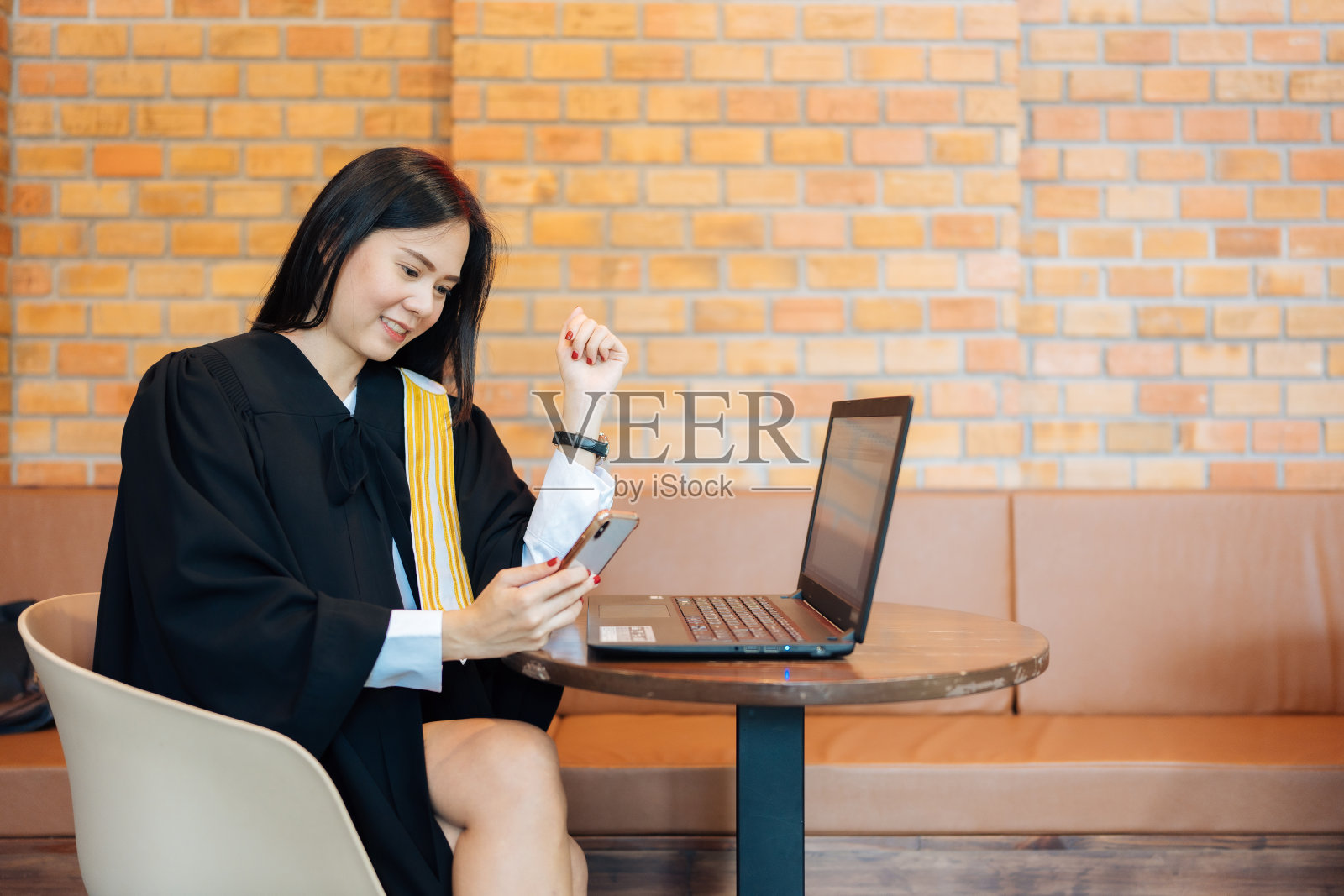 女律师在律师事务所工作时使用智能手机，身穿律师服，使用笔记本电脑咨询和调解原告和被告之间的纠纷照片摄影图片