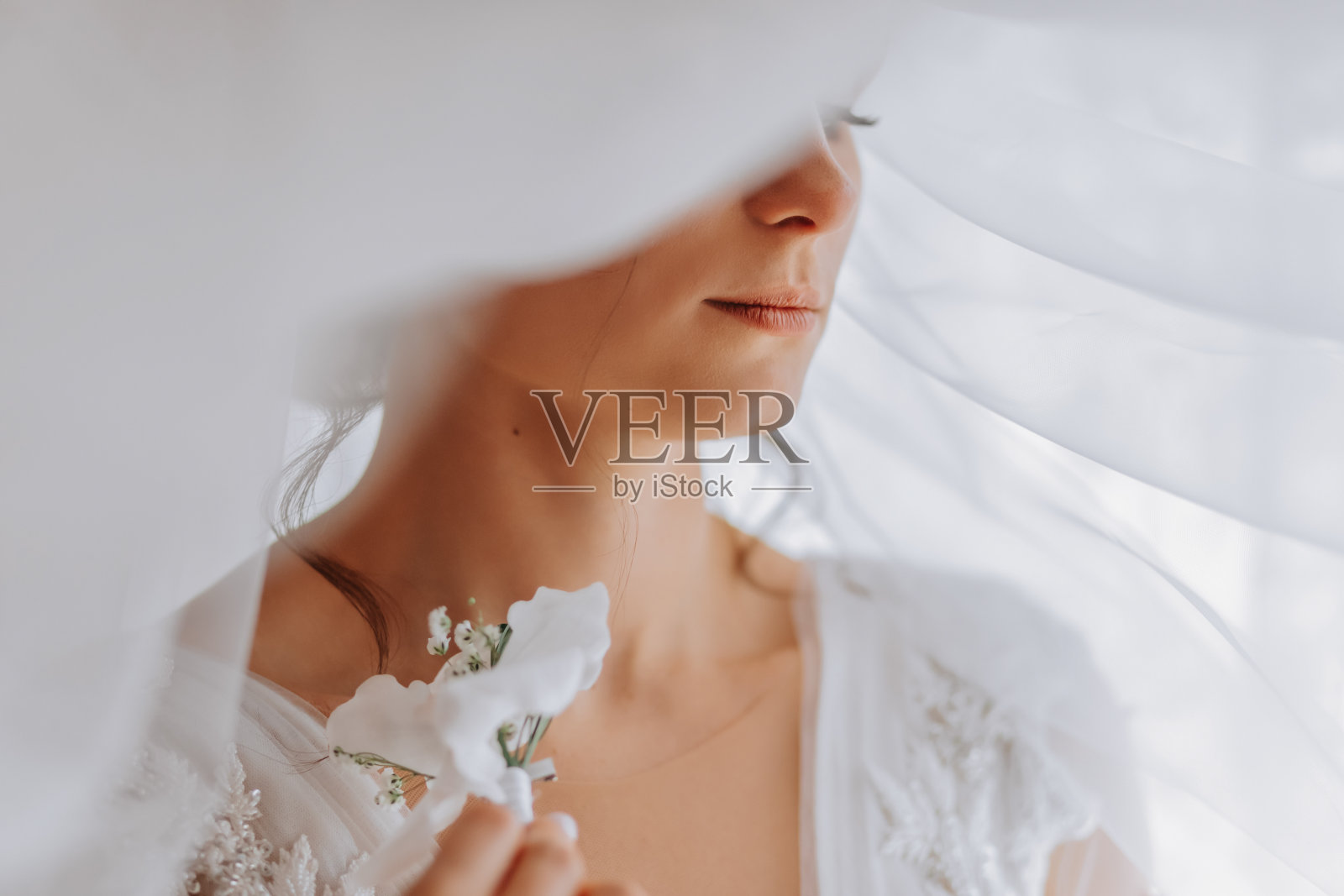 一位身穿白色礼服的黑发新娘手持婚礼花束，摆姿势。法国修指甲。开放的肩膀。美丽的手。长面纱。新娘的早晨。细节照片摄影图片