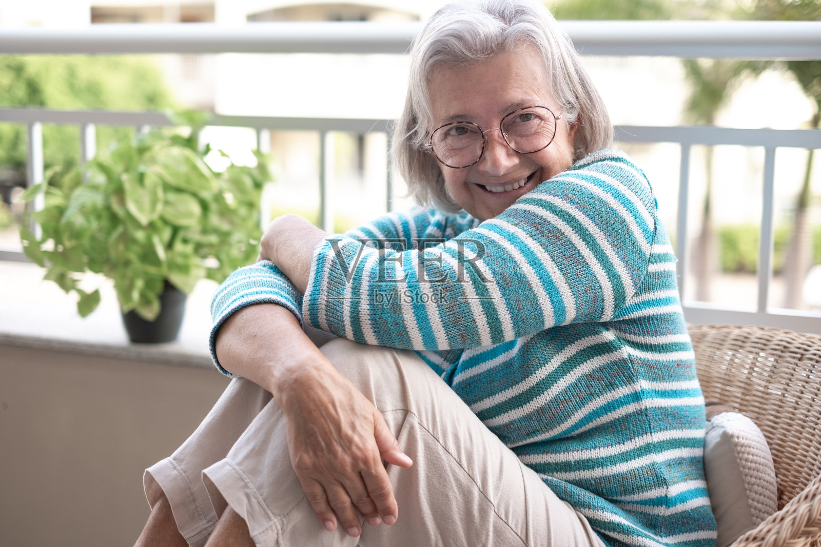 老妇人坐在家里的阳台上享受片刻的放松，戴着眼镜的白发老妇人微笑着看着镜头照片摄影图片