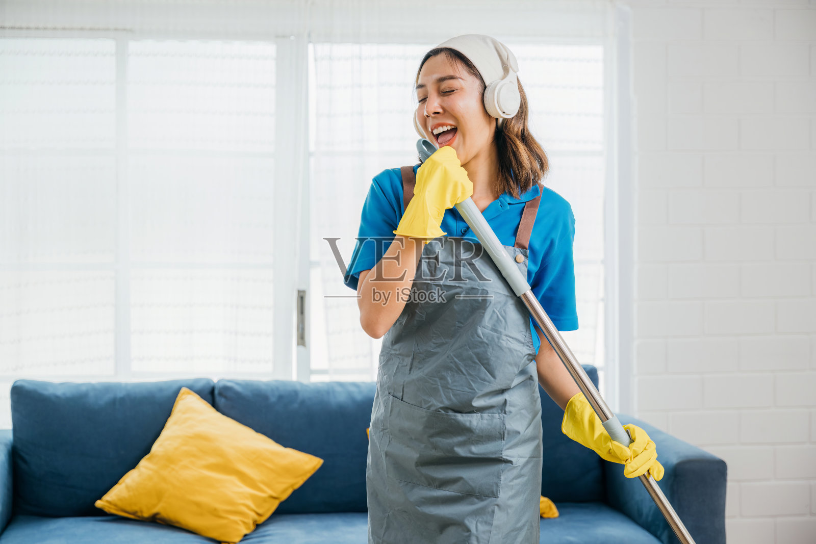 快乐的亚洲家庭主妇在做家务时用拖把当麦克风，一边打扫一边唱着她最喜欢的歌。在客厅里跳舞和打扫，快乐的女仆享受着她的日常生活。照片摄影图片