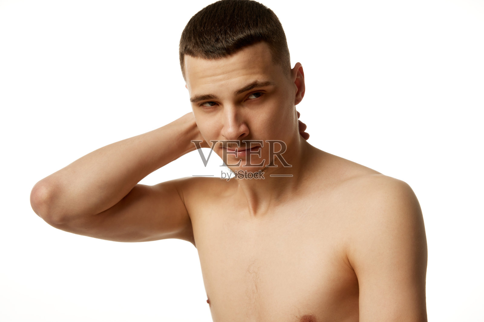 英俊的年轻人把他的手放在脖子上，看着相机在清澈的白色工作室背景。照片摄影图片