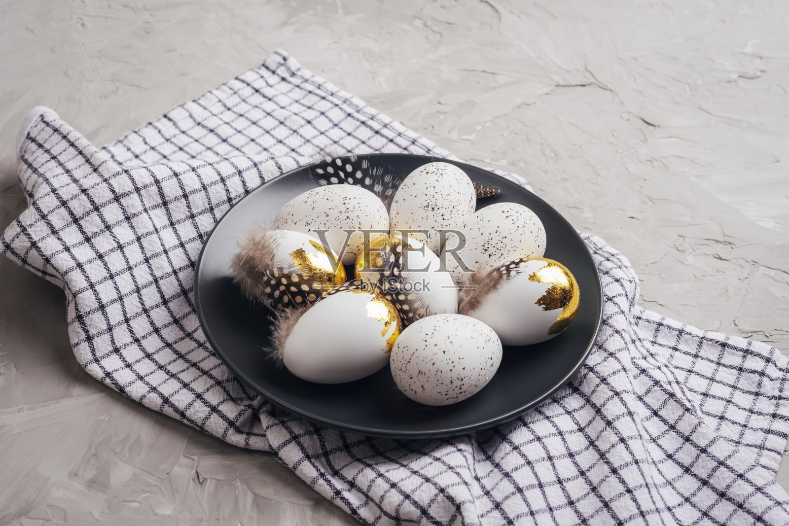 黑色盘子里放着复活节彩蛋，灰色混凝土桌子上放着格子餐巾。俯视图照片摄影图片