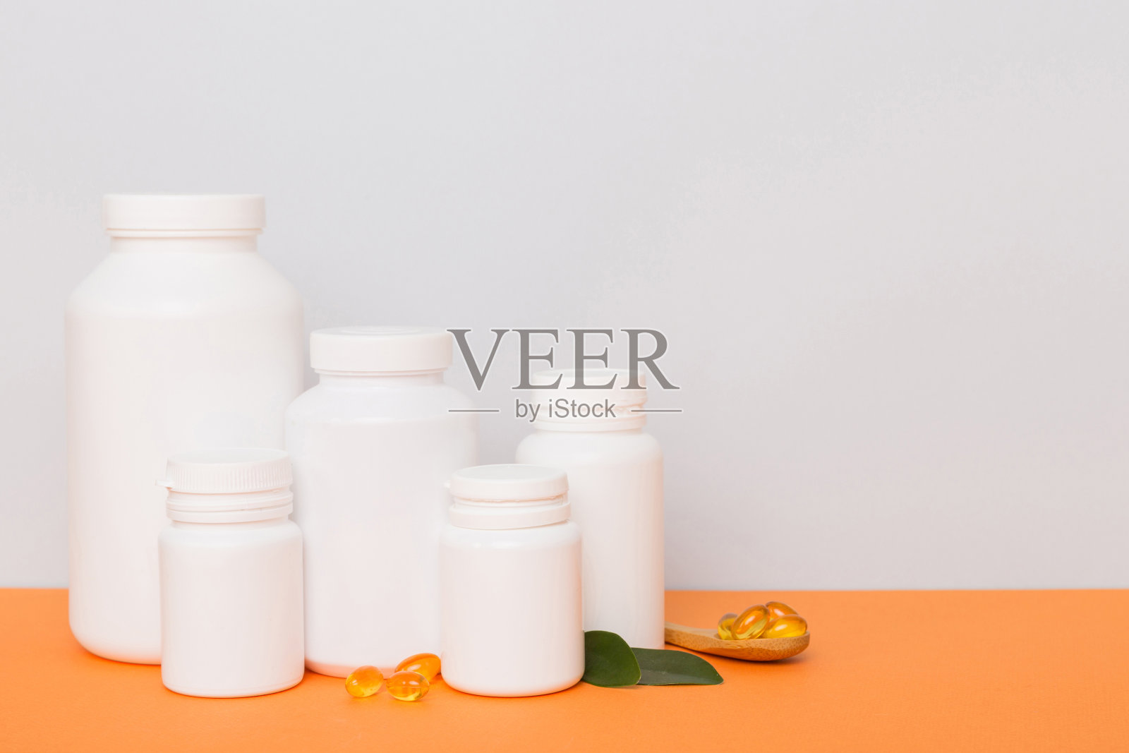 欧米伽-3胶囊装在白色的瓶子里，放在绿叶背景的桌子上。鱼油片。生物活性添加剂。欧米加6欧米加9，维生素A E D，维生素D3上面有复制空间照片摄影图片