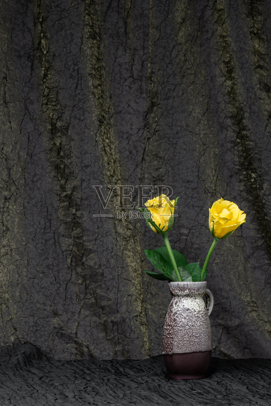 在深褐色布料的背景上，一束美丽的黄玫瑰插在灰色花瓶里。放置文字，复制空间照片摄影图片