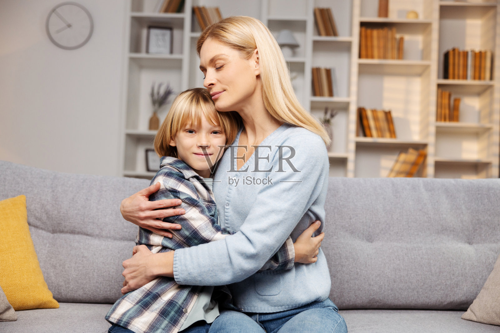 微笑的母亲拥抱着她的小儿子。两人都坐在客厅的沙发上照片摄影图片