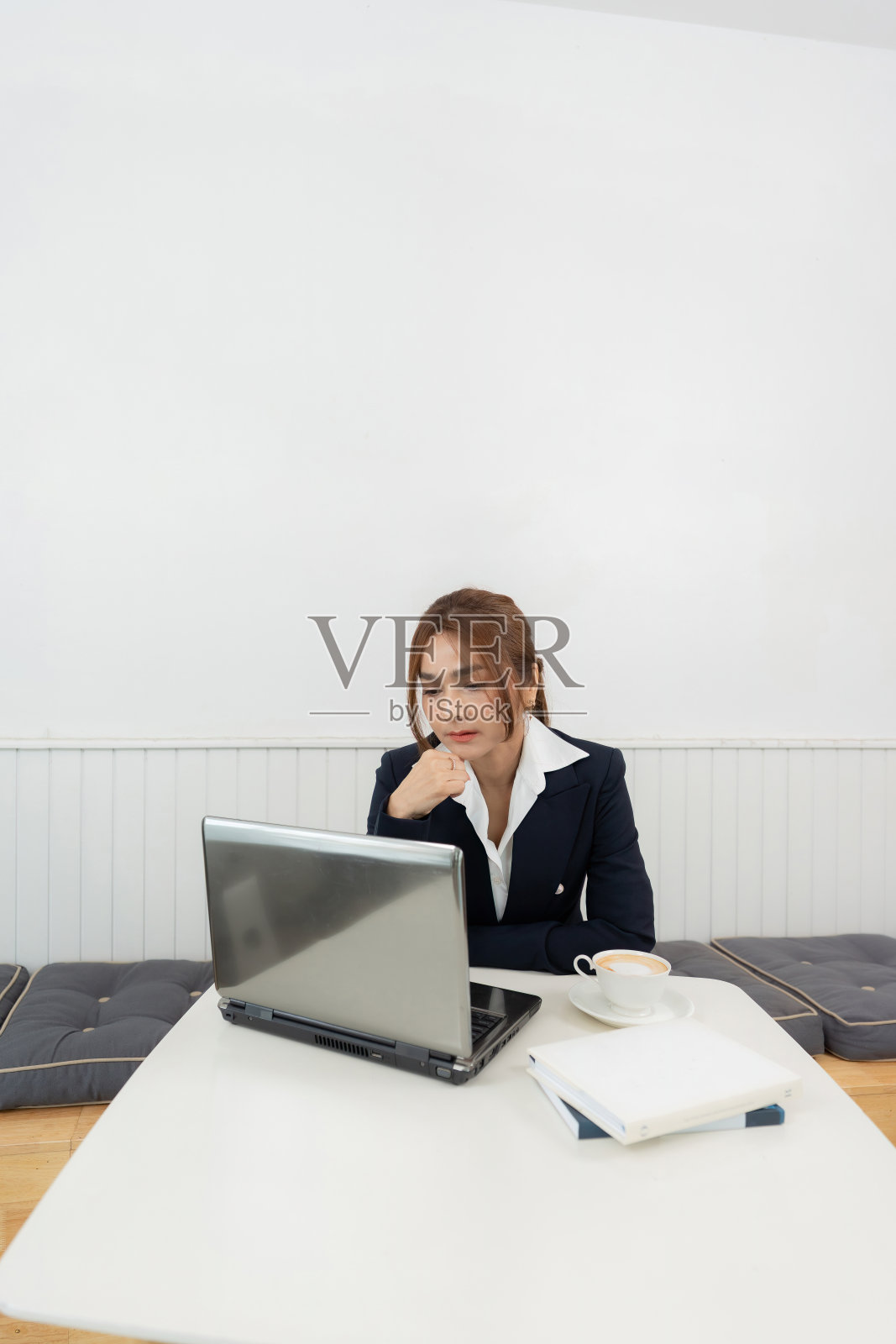 在一家公司的咖啡馆里，穿着西装、留着长发的亚洲女性投资者的垂直形象，笔记本电脑上忧虑的股市下跌和亏损图表，桌子上有一个咖啡杯和一本书。照片摄影图片