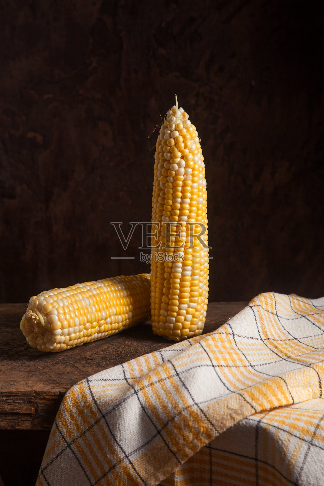 木制背景上的两个甜玉米棒子。照片摄影图片