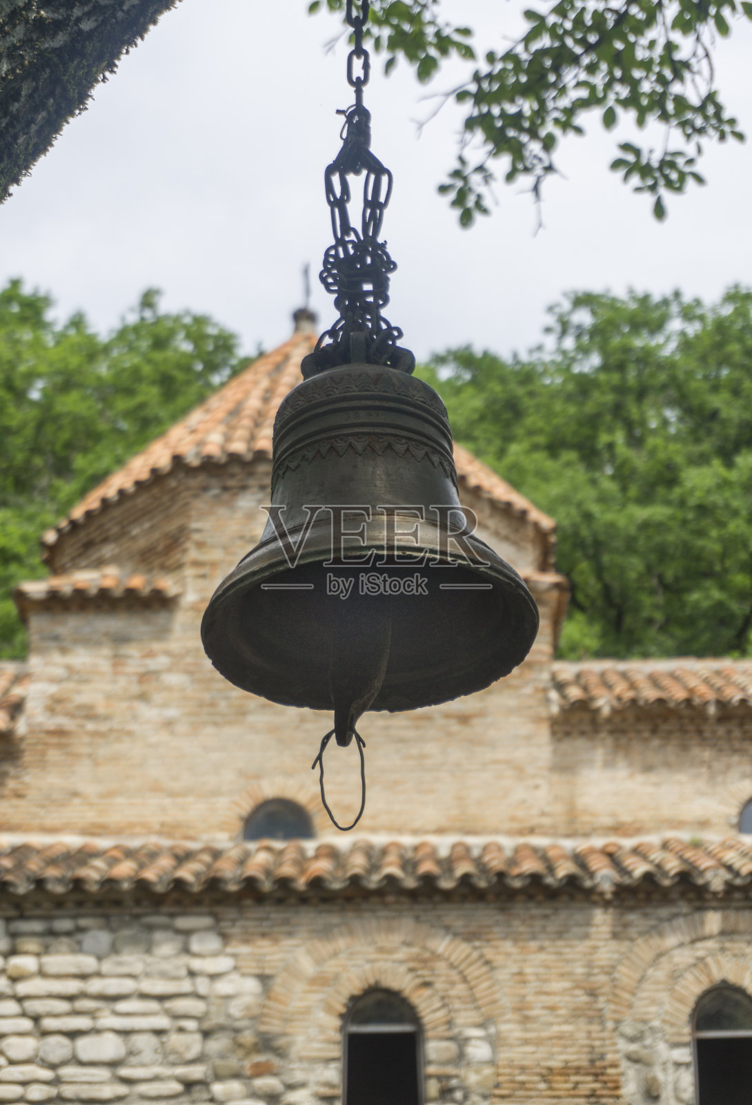 格鲁吉亚Gurjaani Kvelatsminda教堂的两个圆顶和拱形墙前的钟。周围有树和灌木丛。长途跋涉的背景。照片摄影图片