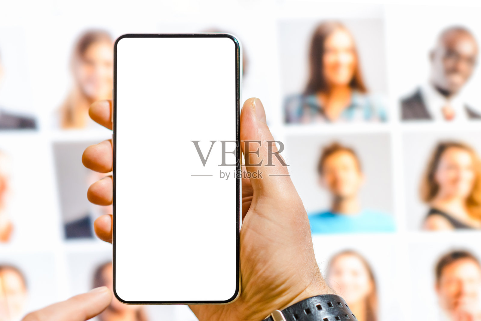 男拿着模拟的白色空白屏幕手机创作。男子使用人工软件在手机上生成逼真的图像。模糊的PC显示器拼贴肖像背景。照片摄影图片