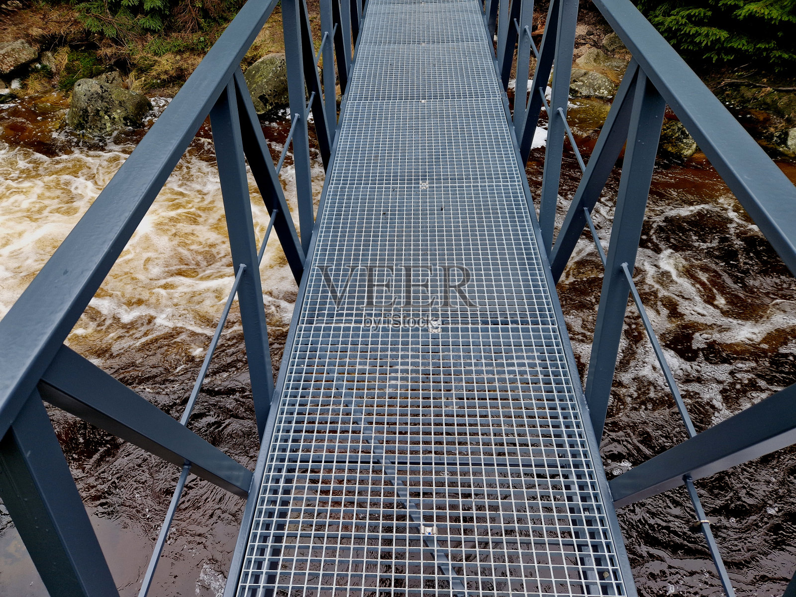 山间河流中狂暴的水元素。毁坏的木桅杆被洪水冲走，撞在岩石上被压得粉碎。这座新的金属桥经久耐用，经得起海浪的冲击照片摄影图片