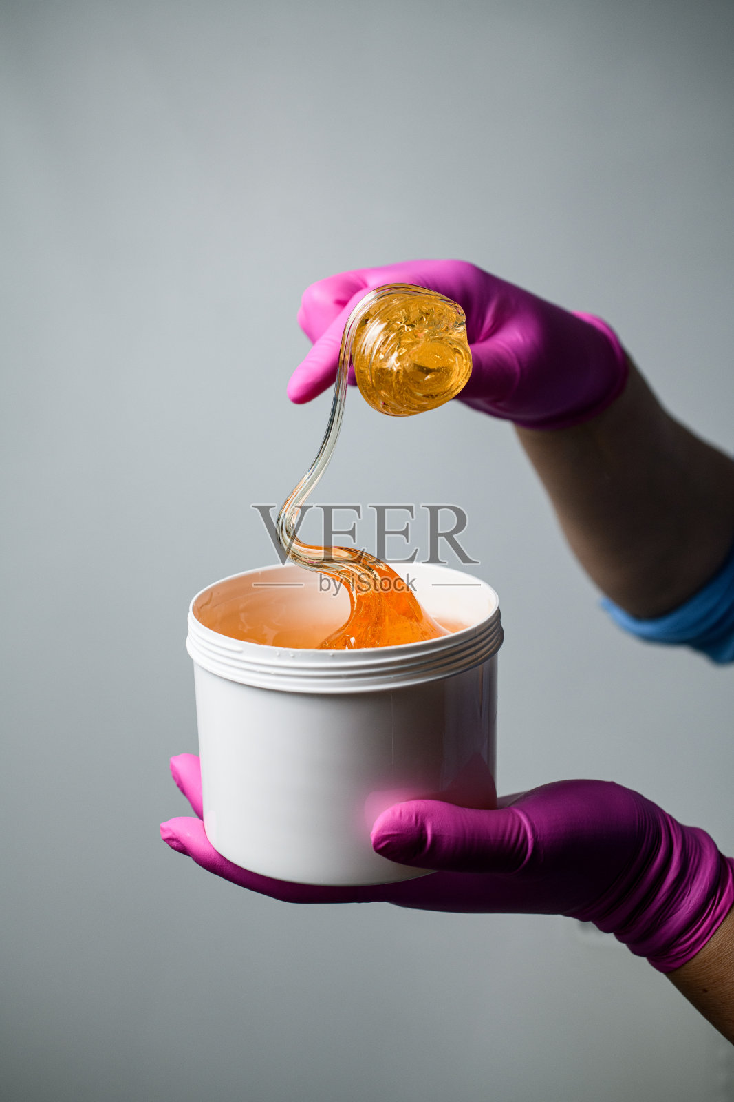 亮黄色的蜜蜡或糖糊在手里，戴着粉红色的橡胶手套照片摄影图片