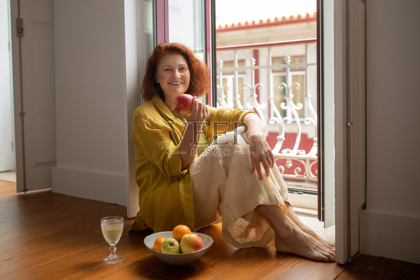 微笑的老妇人坐在敞开的阳台门边，吃着熟苹果照片摄影图片