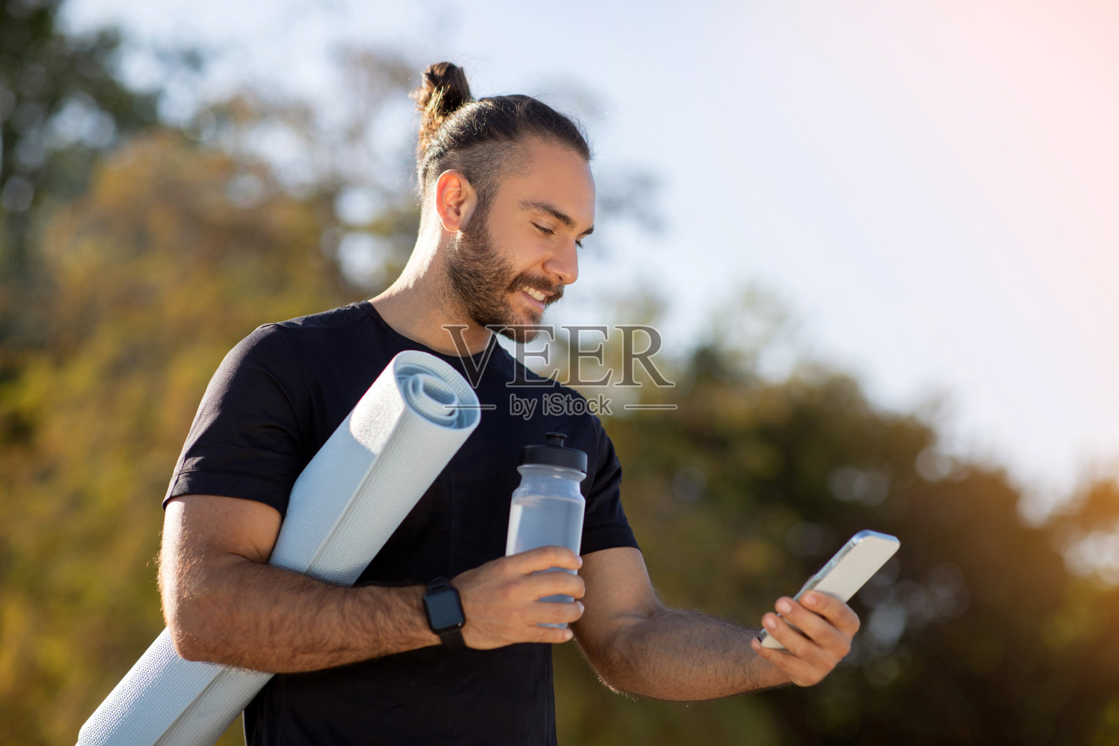 一个人拿着水和垫子站在公园里玩智能手机照片摄影图片