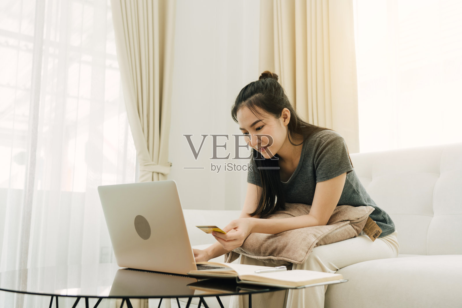 一名亚洲女性在家里度假时，坐在沙发上拿着信用卡网购。照片摄影图片