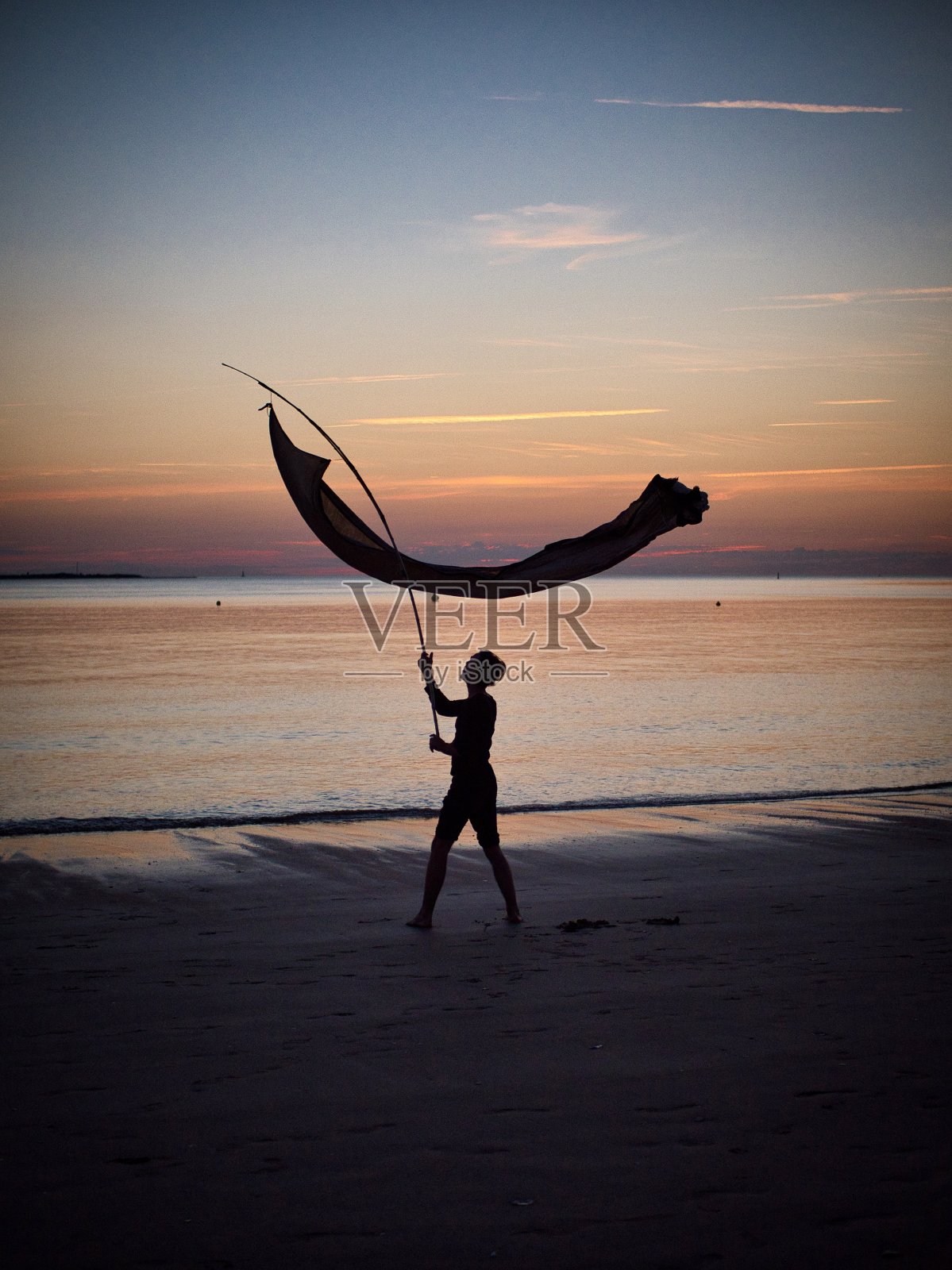 日落时分，一名男子在海滩上挥舞着旗帜照片摄影图片