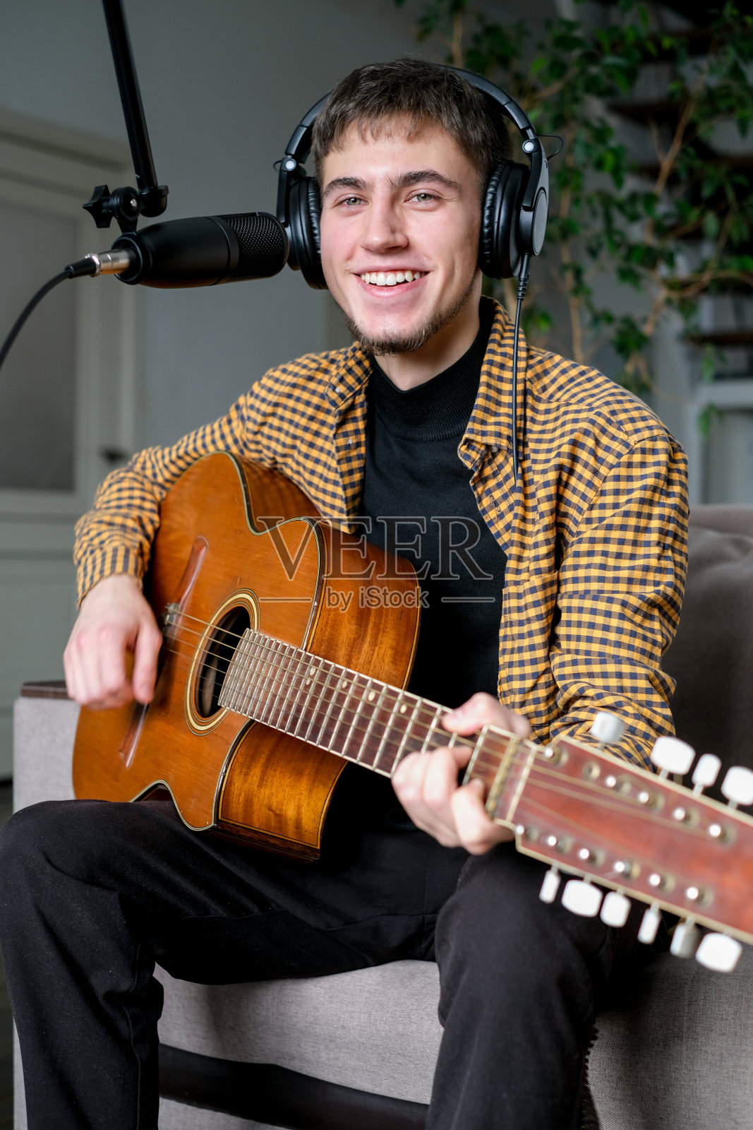 年轻的音乐家在音乐工作室里弹着古典吉他唱歌。男戴着耳机用麦克风唱歌照片摄影图片