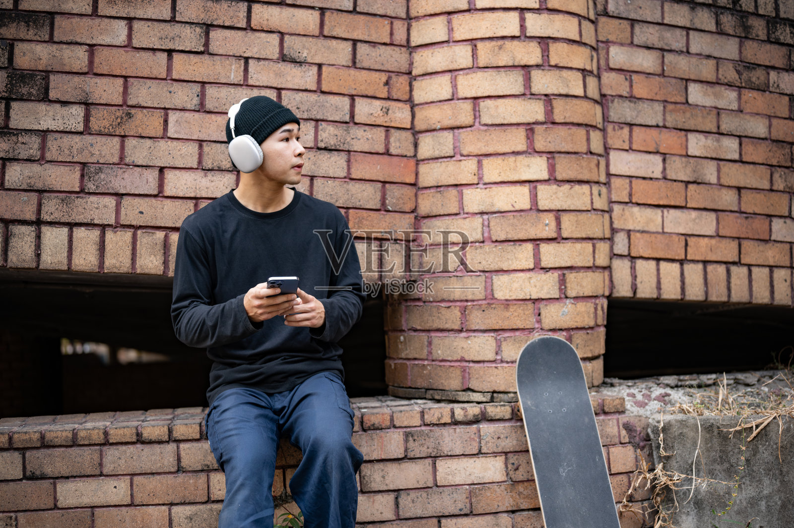 一个很酷的亚洲男性滑冰运动员坐在一座废弃的建筑里，戴着耳机听音乐照片摄影图片