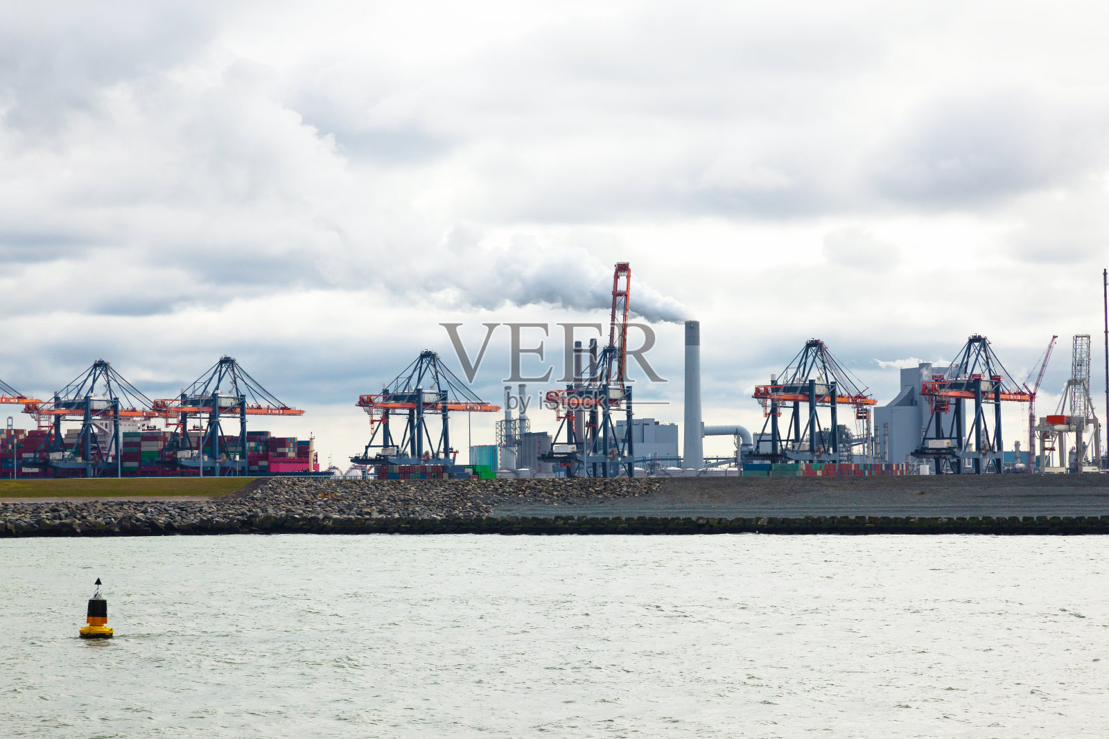 从海湾到集装箱码头，集装箱和集装箱起重机以工业区为背景。照片摄影图片
