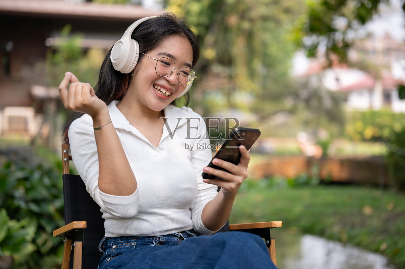 一位快乐的亚洲女性坐在户外，一边听音乐，一边用智能手机。照片摄影图片