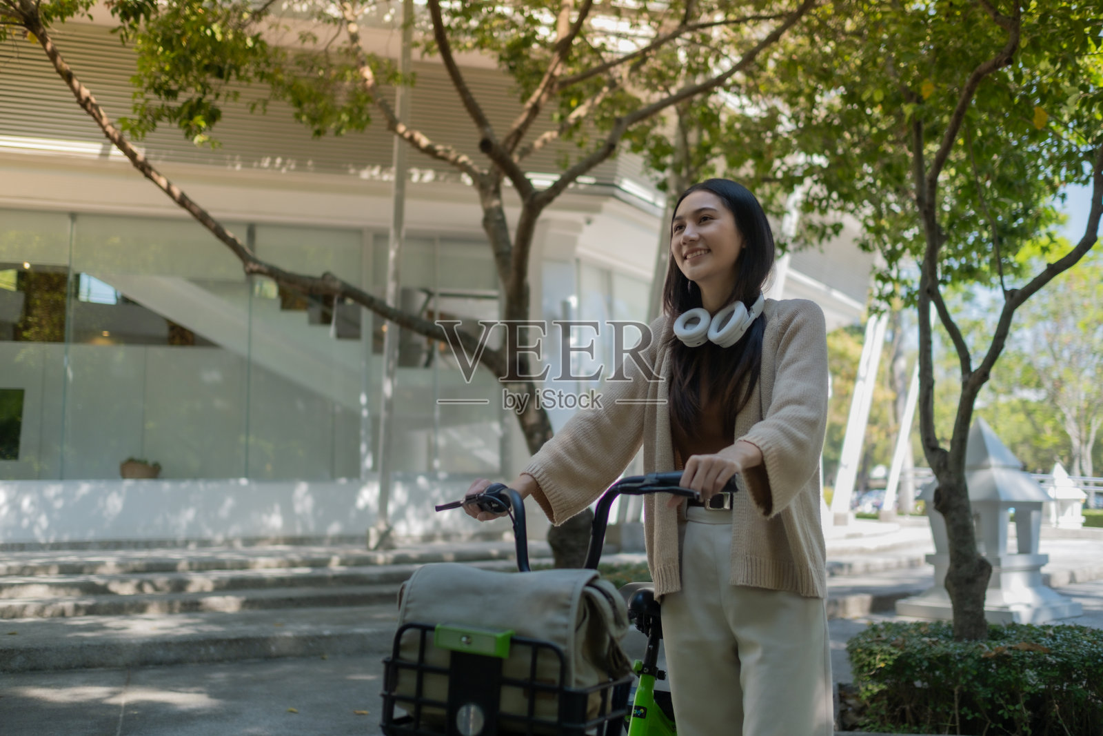 美丽的女人带着耳机和智能手机骑着自行车听音乐，快乐的女人微笑着骑着自行车走在街上，在城市的道路上，生态环境照片摄影图片